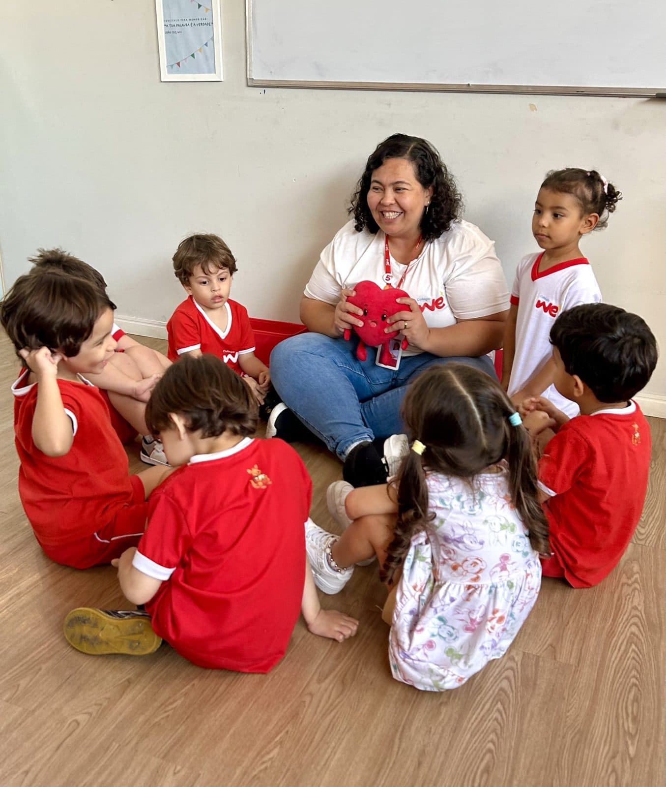 Professora em roda com os alunos segurando um coração de pelúcia